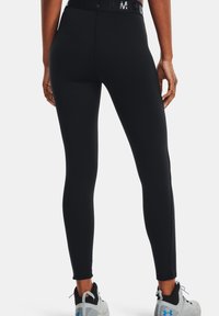 Zwarte leggings met een hoge taille en glanzend logo-detail. Glad oppervlak, aansluitend ontwerp en gestikte patronen bij de enkels.
