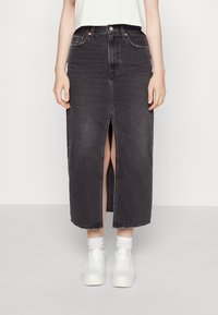 Černá džínová sukně s předním rozparkem a rovým střihem. Disponuje pěti kapsami a kontrastním prošitím. Kombinováno s bílými teniskami.