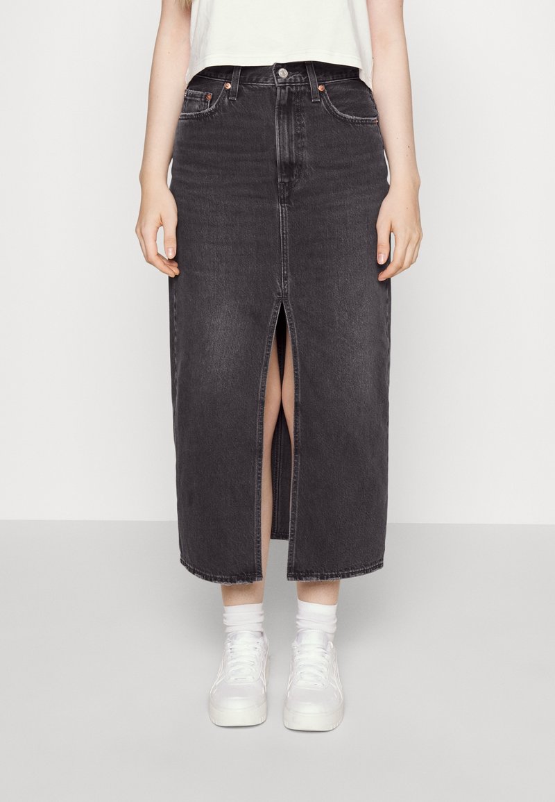 Černá džínová sukně s předním rozparkem a rovým střihem. Disponuje pěti kapsami a kontrastním prošitím. Kombinováno s bílými teniskami.