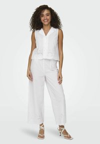 Witte linnen tweedelige outfit bestaande uit een mouwloze blouse met broderie details en wijde broekspijpen. De stof heeft een gladde textuur.
