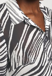 Camicia a righe bianche e nere con colletto indossata da una persona con pelle scura, visibile dal collo fino a metà petto.