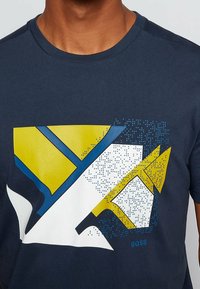 Marinblå bomullströja med grafisk design i gula, blå och vita former, inklusive accenter av prickar och "BOSS"-logotypen.