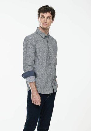 Camicia a bottone grigia a motivo con maniche lunghe arrotolate ai polsini, abbinata a jeans blu scuro. Design semplice e moderno con vestibilità rilassata.