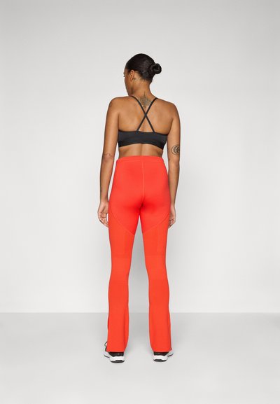 Soutien-gorge de sport noir avec des bretelles croisées, associé à un legging rouge taille haute avec des panneaux texturés et une finition évasée.