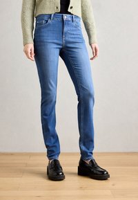 Blauwe spijkerbroeken met een slim fit, vijf zakken ontwerp en een ritssluiting. Draag ze met zwarte platform loafers op een lichte houten vloer.