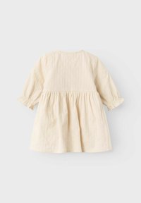 Krämfärgad långärmad babydress med insamlad midja och subtila vertikala ränder, visad mot en ljusgrå bakgrund.