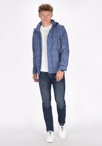 Giacca blu con motivo, dotata di cappuccio, maniche lunghe e zip frontale. Abbinata a una maglietta bianca e jeans scuri, completata con sneakers bianche.