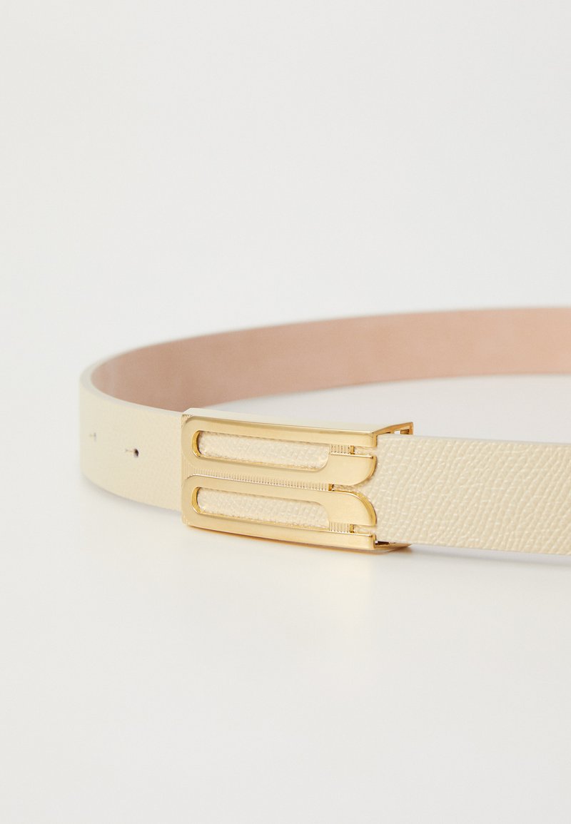 Cinturón de cuero crema con un acabado texturizado. Presenta una hebilla doble en tono dorado y un lado suave en color rosa. Ancho estándar con agujeros ajustables.