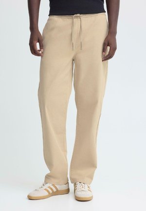 Beige, lichtgewicht, rechte broek met een elastische tailleband en trekkoord, ontworpen voor comfort. Gecombineerd met casual lage sneakers.