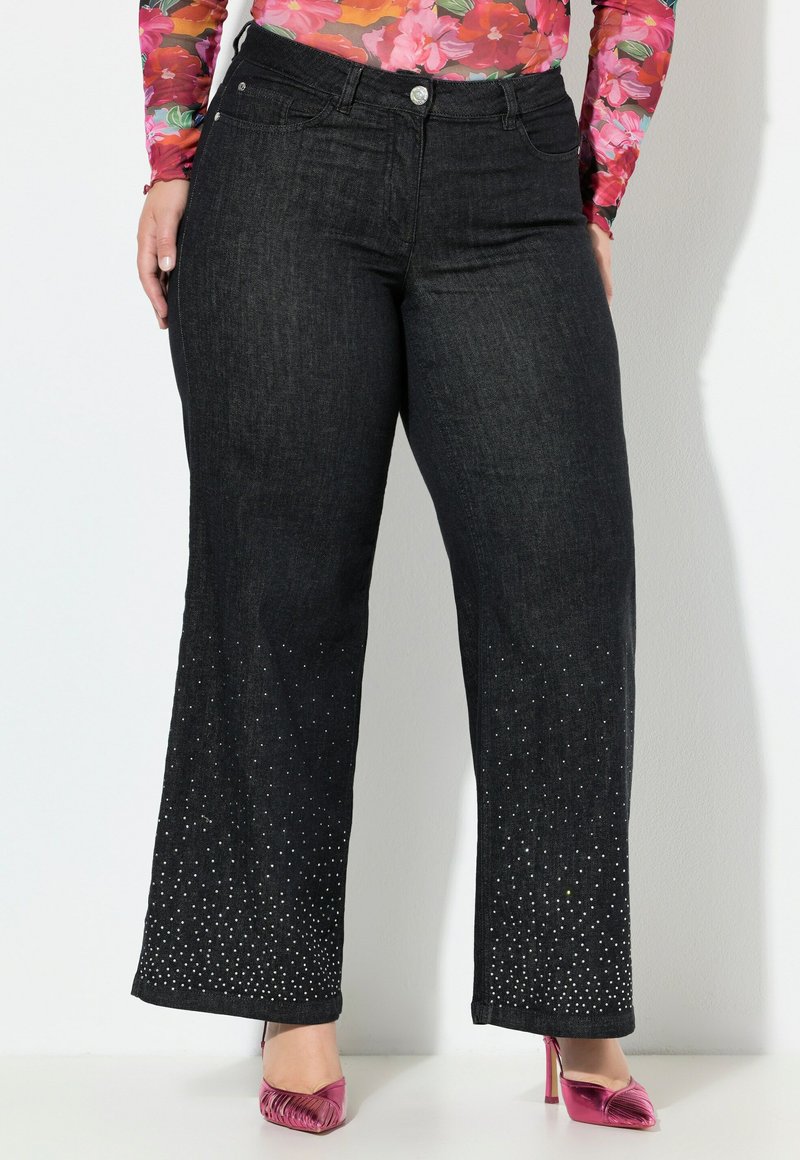 Jeans a gamba larga in denim nero con dettagli di strass all'orlo, abbinati a un top aderente floreale e tacchi rosa.