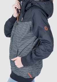 Tmavě modrá bunda s kapucí, která má pruhovaný vzor na přední straně, ribbed manžety a kožené detaily. Obsahuje zipové zapínání a boční kapsy.