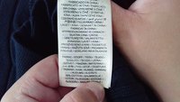 Ręka trzyma metkę odzieżową pokazującą pochodzenie i skład tkaniny w wielu językach, z naciskiem na "Wyprodukowano w Chinach" i "88% bawełny."