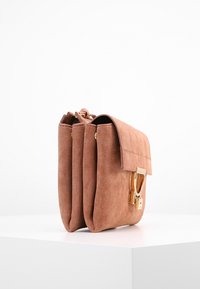 Braune Wildleder-Handtasche mit umgeschlagenem Klappdeckel, ausgestattet mit goldfarbener Schnallenhardware und zwei Fächern, glatte Textur und kompakte rechteckige Form.