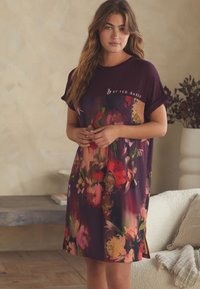 Lila jurk met bloemendessin, gemaakt van zacht materiaal, met korte mouwen en een comfortabele pasvorm. Opvallende bloemen zijn pioenrozen en rozen.