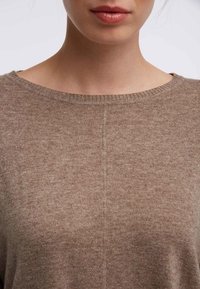 Beige gebreide trui met een brede halslijn, voorzien van een zachte textuur en subtiele steekdetails langs het midden.