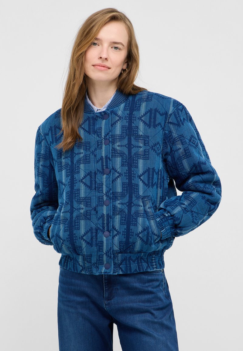 Niebieska pikowana kurtka bomberka z geometrycznymi wzorami, ściągaczami przy mankietach i guzikami. Dwie przednie kieszenie oraz gładkie niebieskie podszycie.