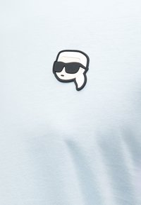 Χαλάκι σε φωτεινό μπλε ύφασμα με λεία υφή, που απεικονίζει ένα μαύρο και άσπρο λογότυπο από καουτσούκ ενός χαρακτήρα με γυαλιά ηλίου.