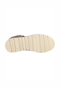 Semelle d'une chaussure avec une surface en caoutchouc beige texturée comportant des stries et des rainures pour la traction, montrant une forme plate et arrondie.