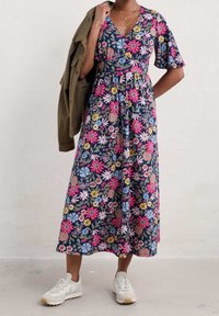 Robe midi florale avec fond marine, ornée de fleurs roses, bleues et jaunes. Décolleté en V, manches courtes, associée à une veste verte et des baskets blanches.