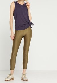 Lila ärmlös topp med knutdetalj vid midjan, i kombination med olivgröna leggings. Beiga träningsskor fulländar outfiten.