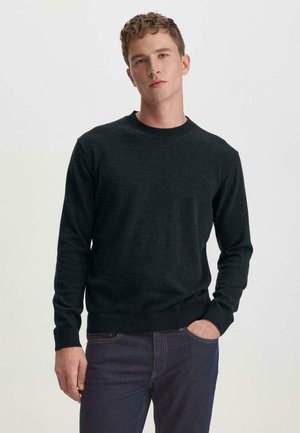 Donkergrijze, gebreide trui met een ronde hals en lange mouwen. Geribbelde manchetten en zoom, zachte textuur, gedragen over donkere jeans.