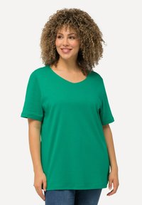 Grøn T-shirt med korte ærmer og v-hals, blød tekstur og afslappet pasform, båret med blå jeans imod en lys baggrund.