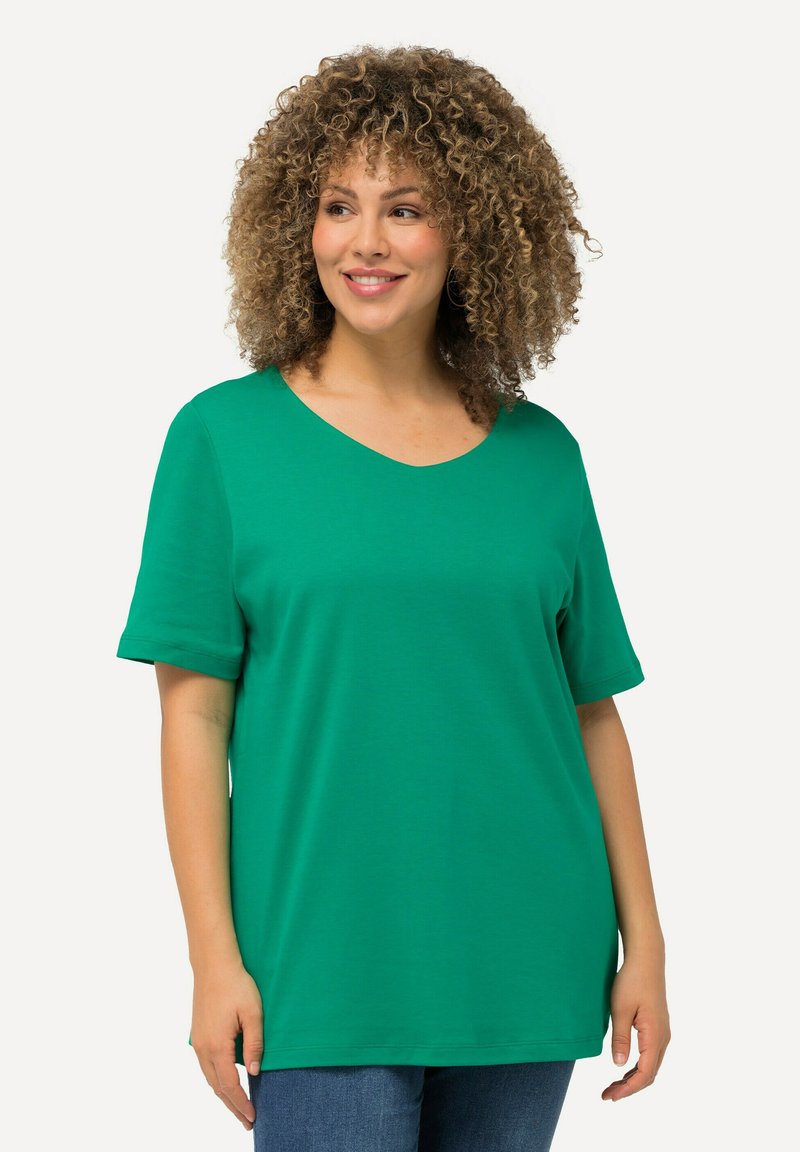 Grøn T-shirt med korte ærmer og v-hals, blød tekstur og afslappet pasform, båret med blå jeans imod en lys baggrund.