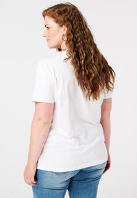 Korte mouw, wit katoenen t-shirt met een ronde hals, gecombineerd met lichtblauwe denim jeans. Haar in losse, golvende krullen.