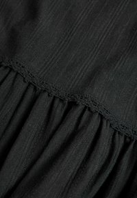 Tissu noir avec nervures verticales et une couture froncée ornée d'une fine bordure en dentelle.