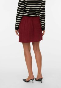 Jupe en velours côtelé rouge avec une taille élastique, associée à un haut rayé noir et blanc. Porte des escarpins à pois noirs.