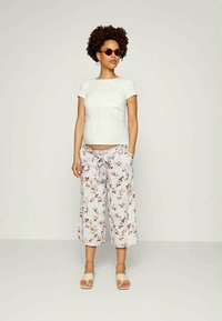 T-shirt branca ajustada combinada com culottes de padrão floral em azul claro com cintura ajustável. O modelo usa óculos de sol redondos e sandálias leves.