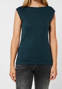 Turkos ärmlös topp med båthals, tillverkad av mjukt tyg, med en figurnära design och en slät textur. Bärs med grå denim.