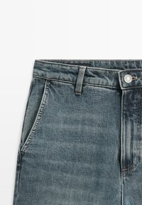 Jeans in denim azzurro chiaro con taglio dritto, dotati di tasche frontali, chiusura con bottone e sfumature sottili per la texture.