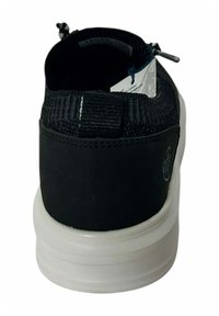 Zapatilla deportiva negra con parte superior texturizada, talón negro liso y suela blanca. Presenta una pestaña para tirar y una etiqueta en el interior para la identificación de la marca.