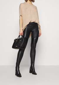 Beżowy sweter z dzianiny, czarne legginsy z sztucznej skóry oraz czarna torebka. Legginsy mają prążkowane akcenty. Modelka nosi czarne botki na obcasie.