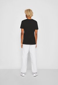 Black short-sleeve t-shirt, cotton fabric, round neckline, paired with white wide-leg pants and sneakers, viewed from the back.