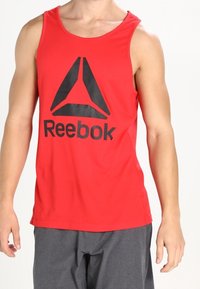 Débardeur rouge sans manches en tissu léger, arborant un grand logo Reebok noir sur le devant. Design simple et coupe décontractée.
