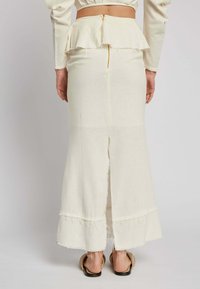 Long cream-colored skirt made of textured fabric. Features a frayed hem, a side slit, and a zip closure at the back.