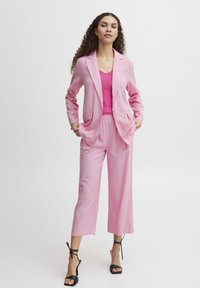 Pink linen suit featuring a fitted blazer with two front pockets and relaxed-fit cropped pants. Paired with pink knit top and black heeled sandals.
