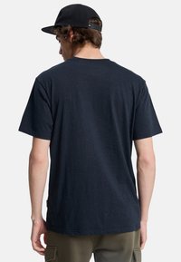 Camiseta azul marino con textura moteada, de manga corta y cuello redondo, combinada con pantalones cargo verde oliva.