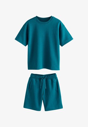 Tirkīzzils īsroku T-krekls un atbilstoši elastīgi vidukļa šorti ar auklas aizdari, izklāti uz balta fona.