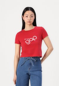 Rode crop top met korte mouwen en een ronde hals, voorzien van een witte logo-opdruk. Gecombineerd met hoge, blauwe spijkerbroeken.