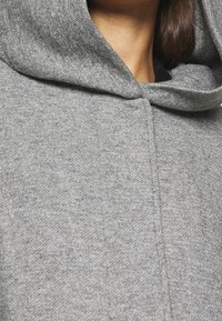 Grå hoodie med ett mjukt, strukturerat tyg, stor rund huva och enkel sömdetaljering, vilket ger en tight passform.