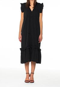Musta mekko, jossa on lyhyet puffihihat, V-pääntie, koristeelliset napit ja röyhelöhelma. Yhdistetty mustiin nauhakenkiin.