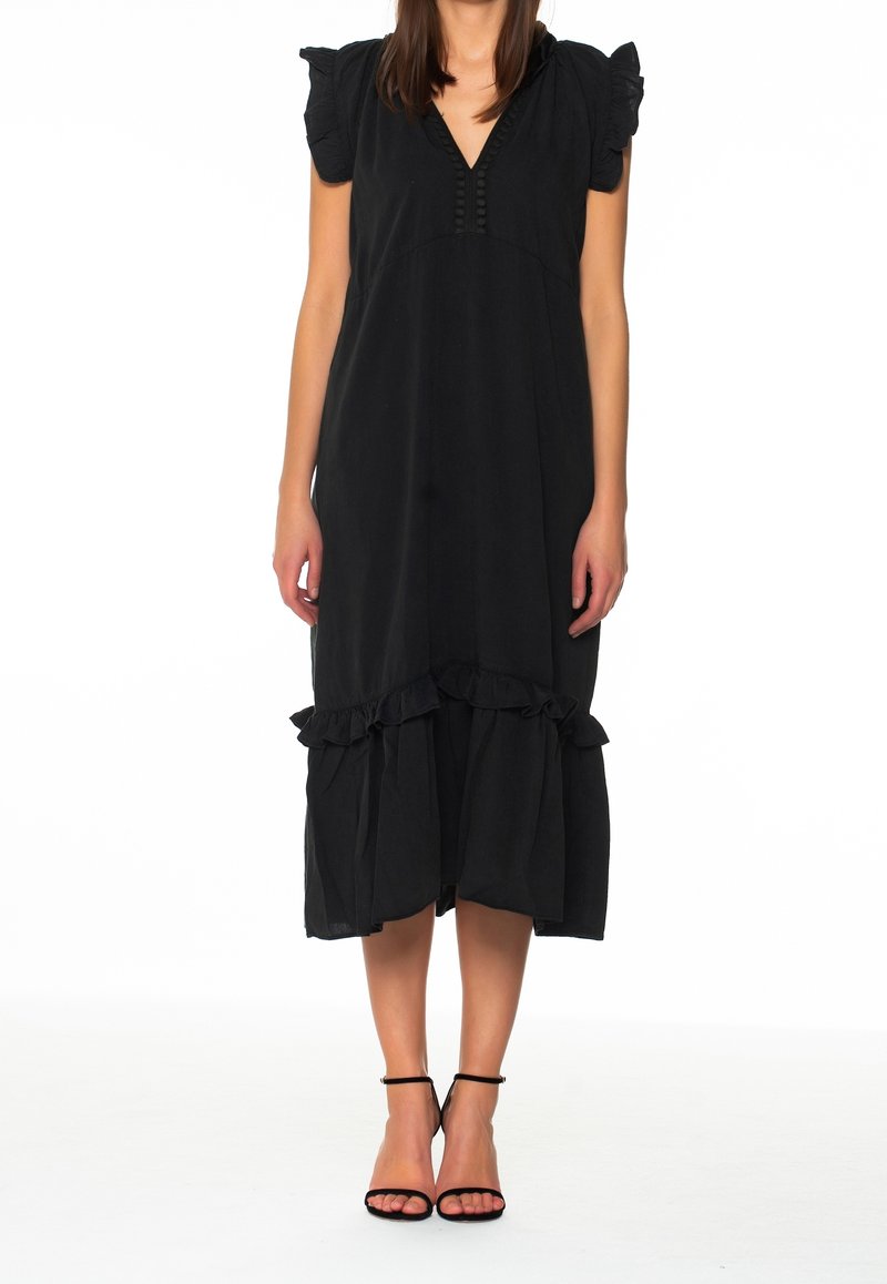 Musta mekko, jossa on lyhyet puffihihat, V-pääntie, koristeelliset napit ja röyhelöhelma. Yhdistetty mustiin nauhakenkiin.