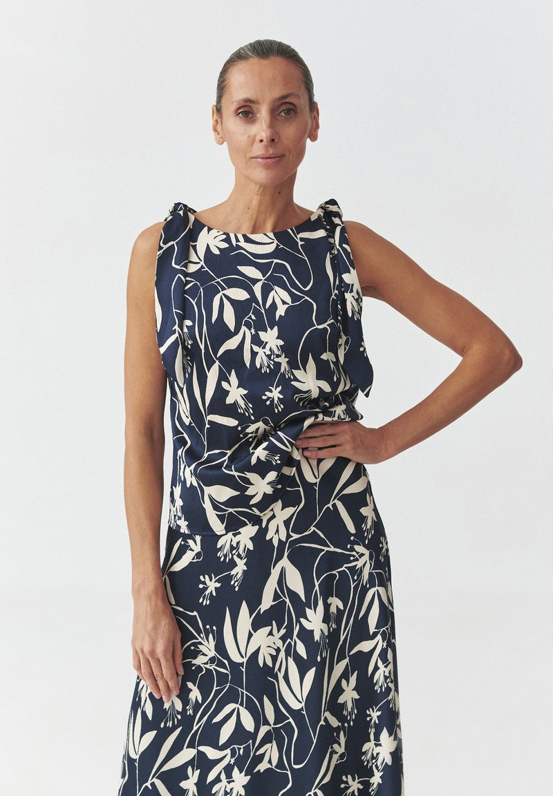 Rochie bleumarin cu modele florale albe, având bentițe la umeri și un detaliu de talie legat. Fabricată dintr-un material texturat.