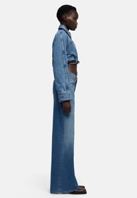 Krótka kurtka jeansowa z długimi rękawami, zestawiona z wysokim stanem, szerokimi spodniami jeansowymi. Oba elementy wykonane są z jasnoniebieskiego denimu z efektami wyblaknięcia.