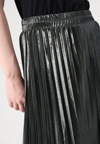 Fustă plisată metalică de culoare gri închis, având un waistband elastic și o textură netedă. Plisările creează un model ritmic pe întreaga țesătură.