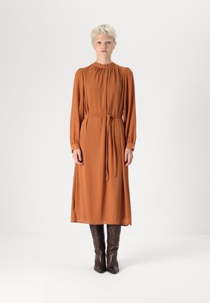 Bronze long-sleeved dress with gathering at the neckline and a tied waist, paired with brown leather knee-high boots featuring intricate stitching.