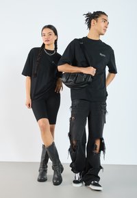 Zwarte oversized t-shirts, zwarte biker shorts, versleten zwarte jeans, kniehoge zwarte laarzen met studs en een zwarte crossbody bag.